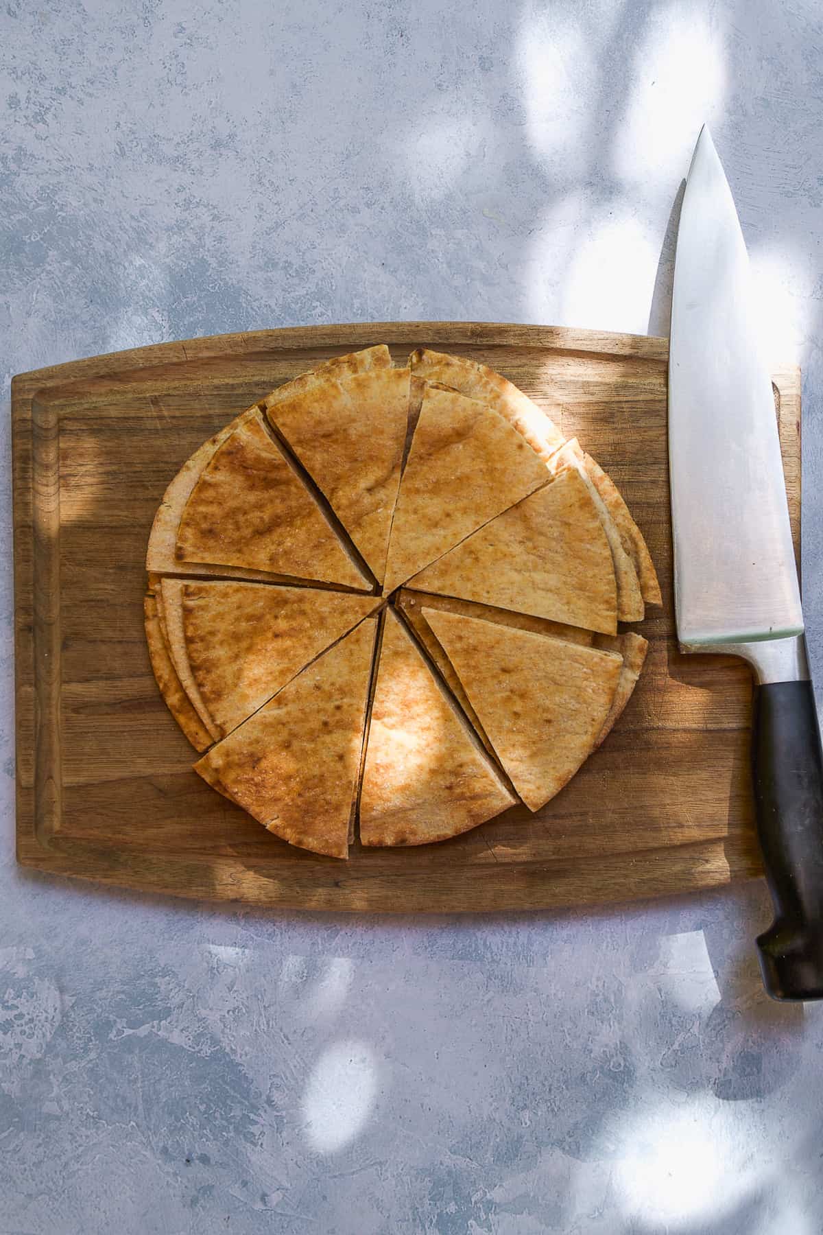 Overhead view of pita being cut into triangles on a wooden cutting board.