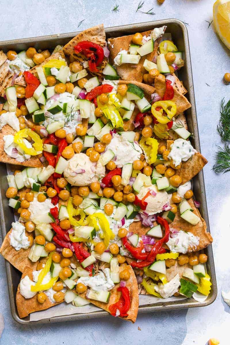 Greek nachos on a sheet pan on a blue surface.