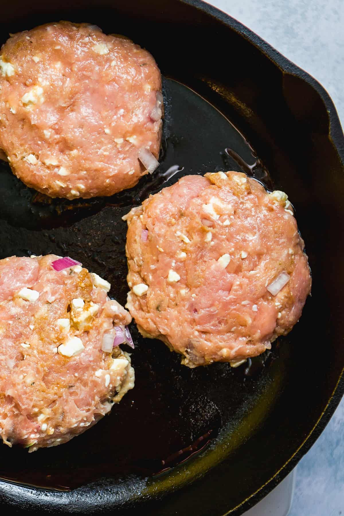 Chicken burgers cooking on a cast iron skillet.