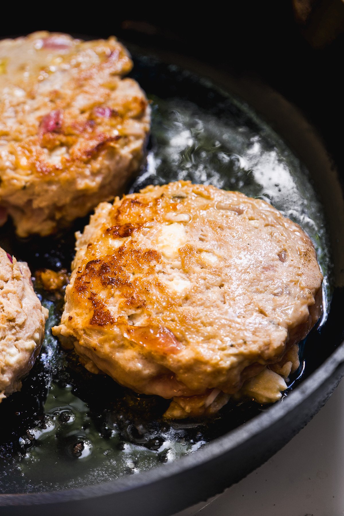 Cooked chicken burgers in a black cast iron pan.