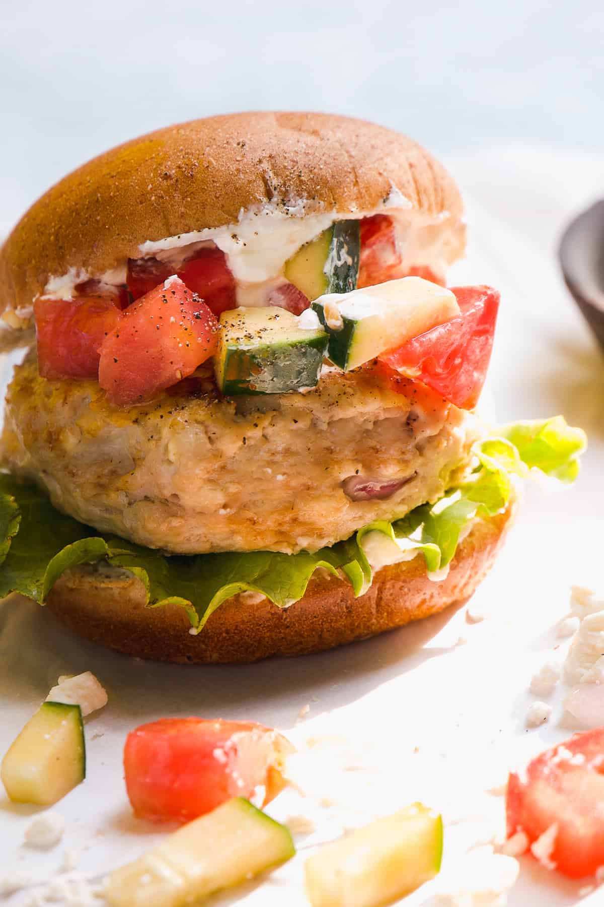 Chicken burger with a bun and cucumber and tomatoes on top.