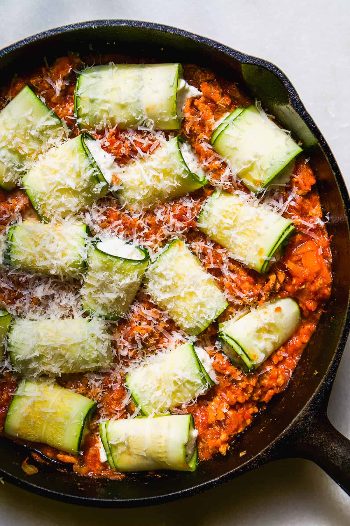 Zucchini lasagna roll ups with cheese about to be baked in a cast iron skillet.