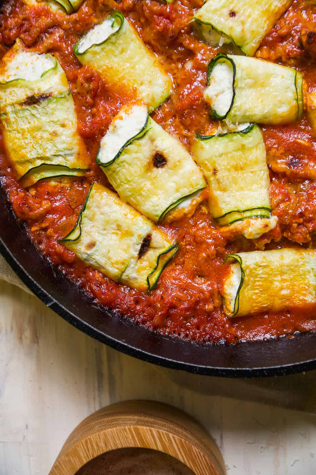 Rolled up zucchini and cheese in tomato sauce in a black pan.