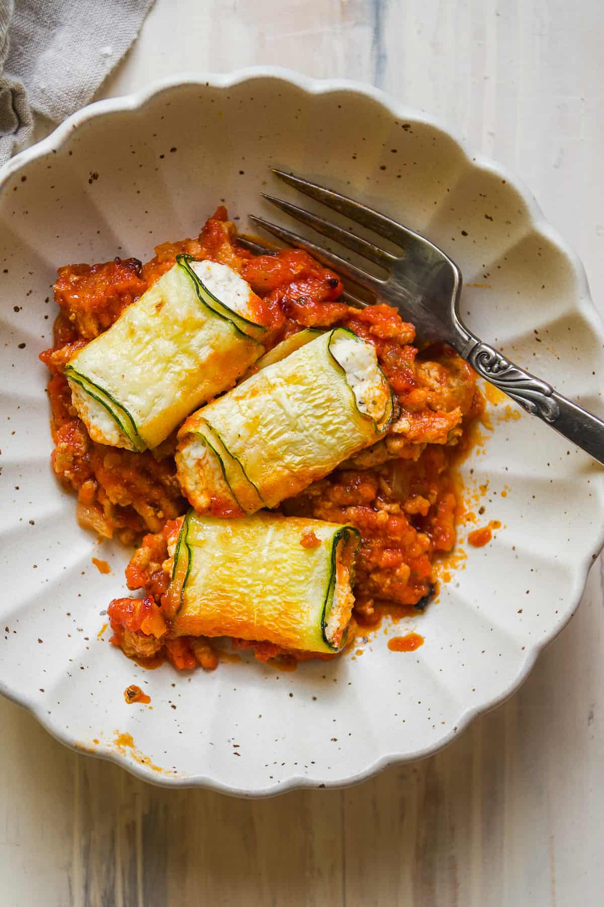 Gray bowl with tomato sauce and three pieces of zucchini cheese roll ups.