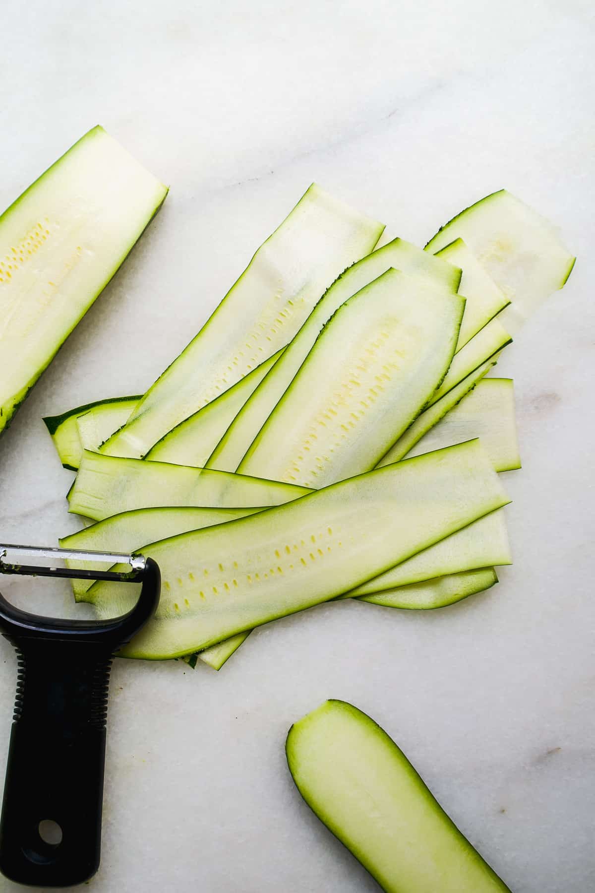 Thin slices of zucchini cut on a marble cutting board.