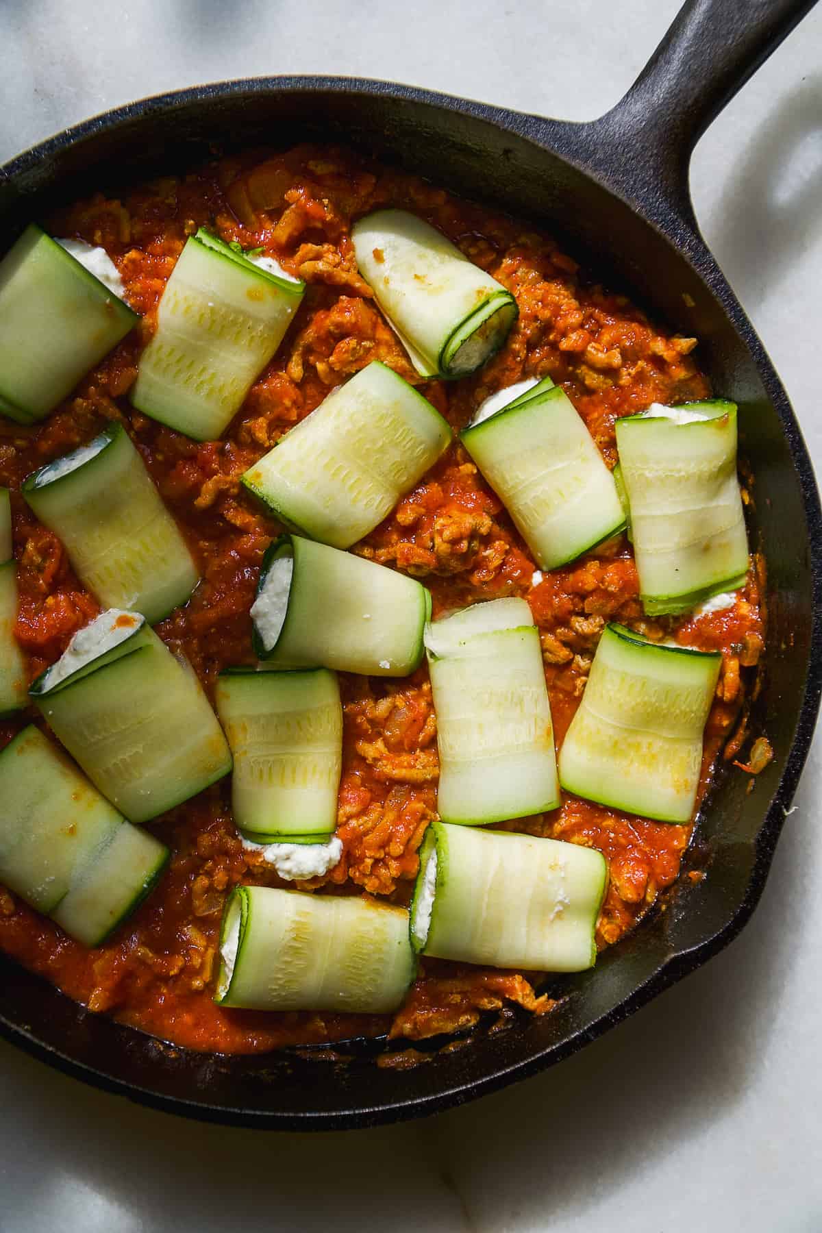 Zucchini involtini about to be cooked in a black pan.