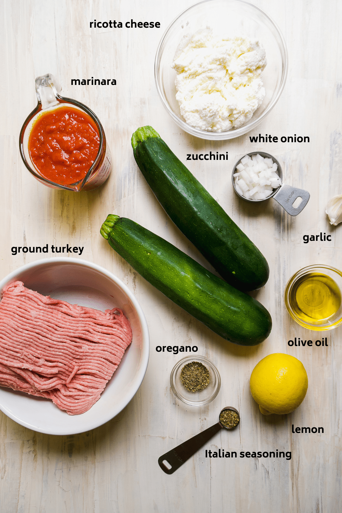 Zucchini involtini ingredients on a white surface with labels in black.