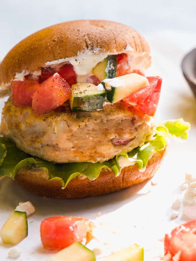 Chicken burger with a bun and tomato and cucumbers on top.