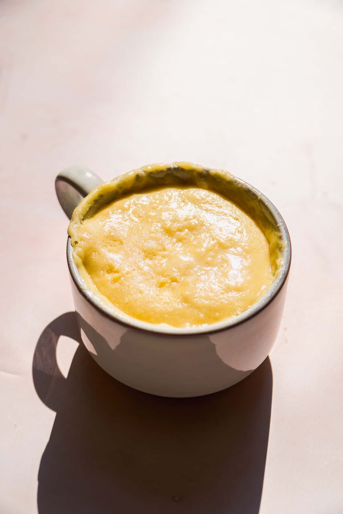 Baked lemon mug cake on a pink surface.