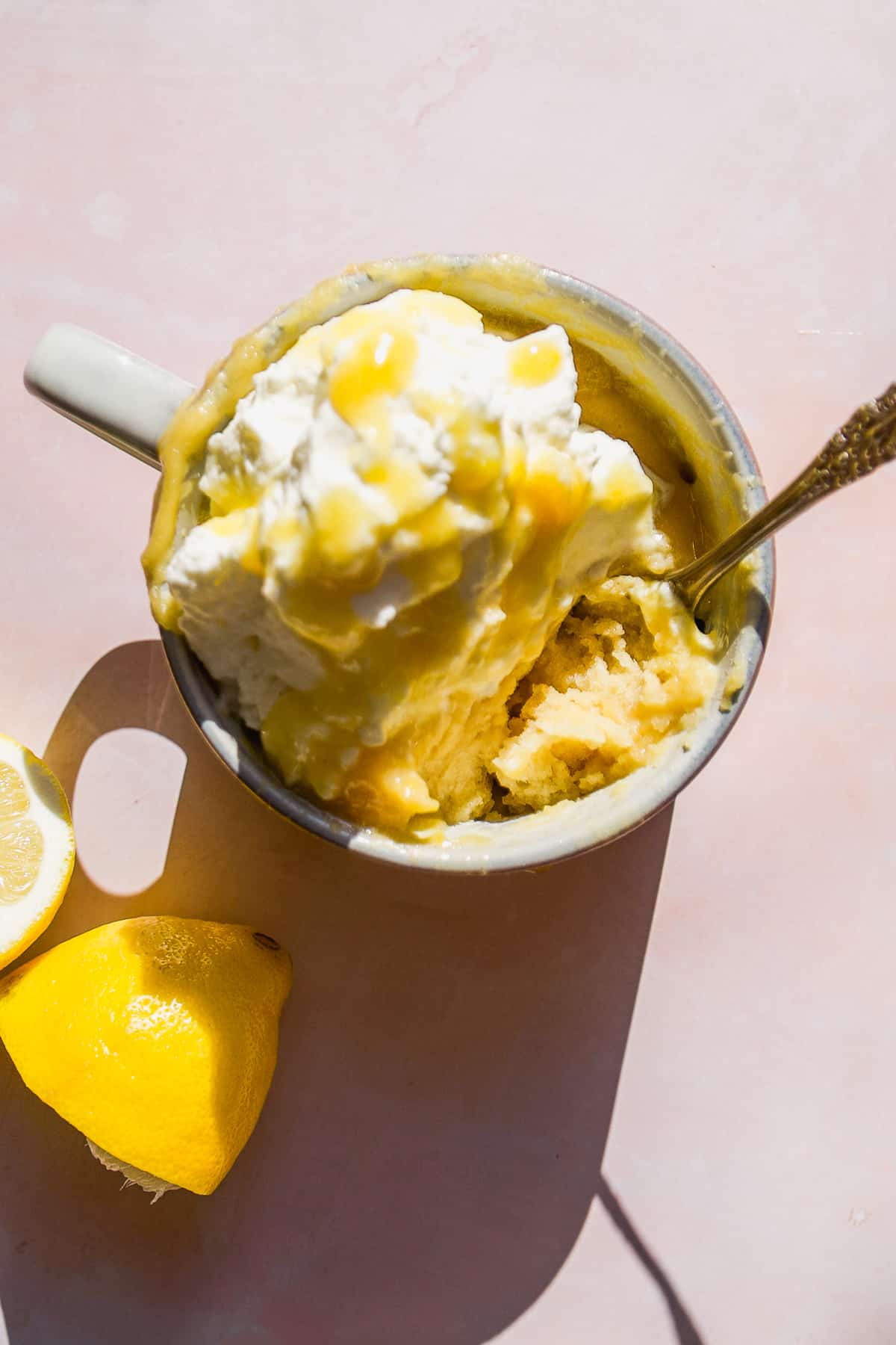 Overhead view of a mug of lemon cake with whipped cream on top.