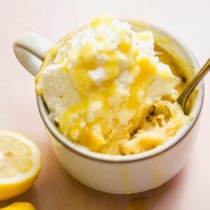 Lemon mug cake in a coffee mug with whipped cream and lemon curd on top.