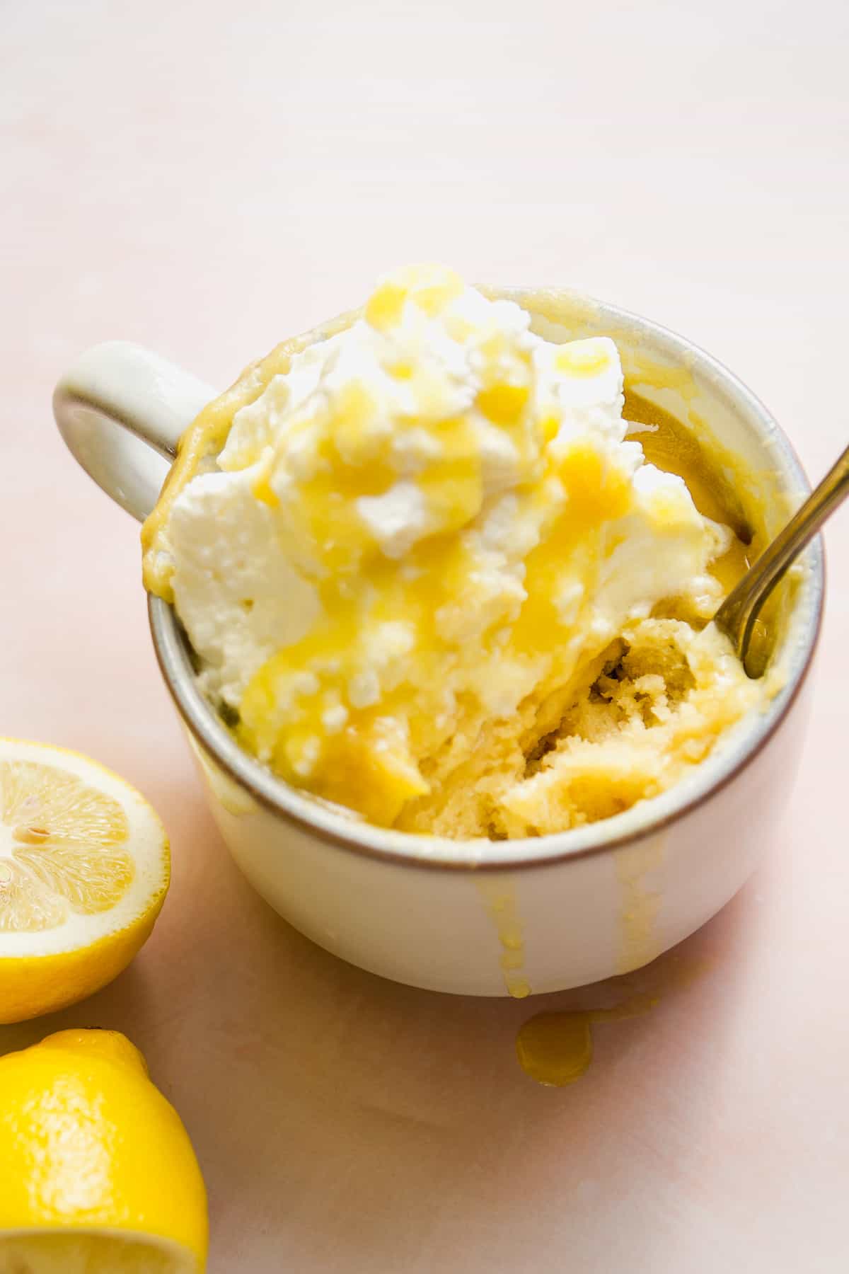 Lemon mug cake with whipped cream on a pink surface.