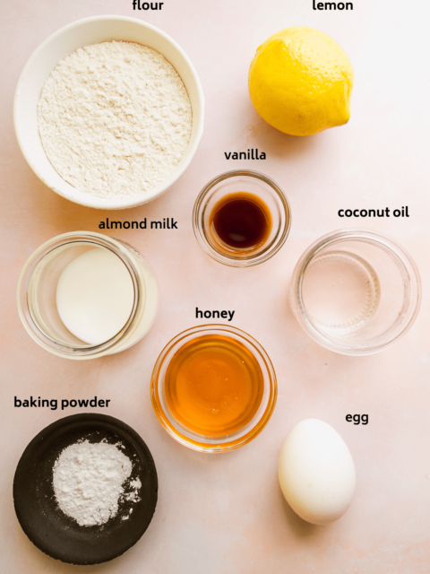 Lemon mug cake ingredients on a pink surface with labels in black.