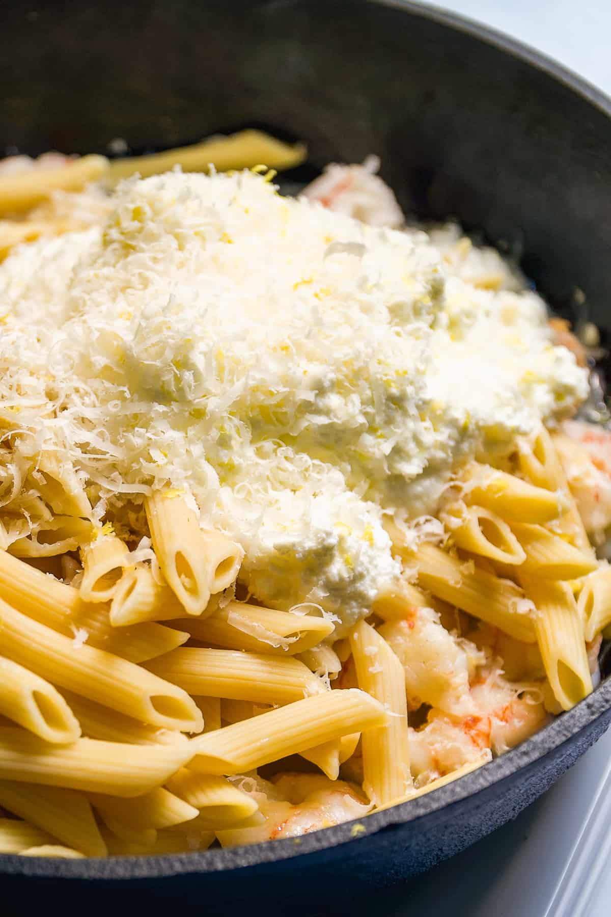 Pasta in a cast iron pan with ricotta and parmesan on top about to be mixed.