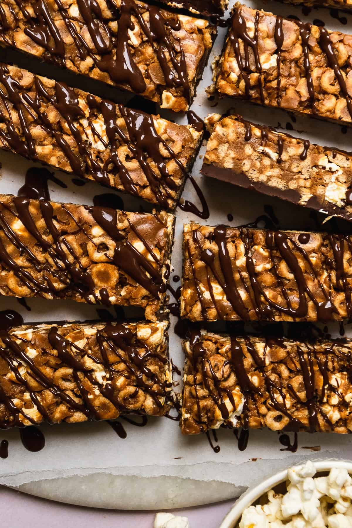 Rectangular peanut butter cheerio bars with chocolate drizzled on top on parchment paper.