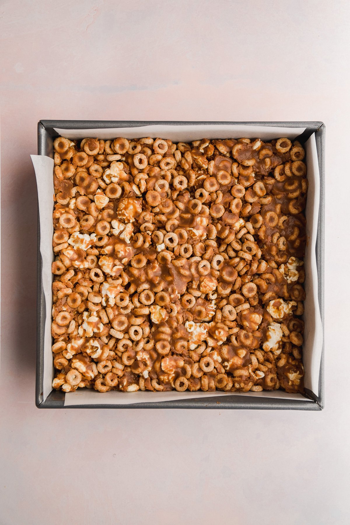 Square baking pan with peanut butter cheerio mixture pressed inside.