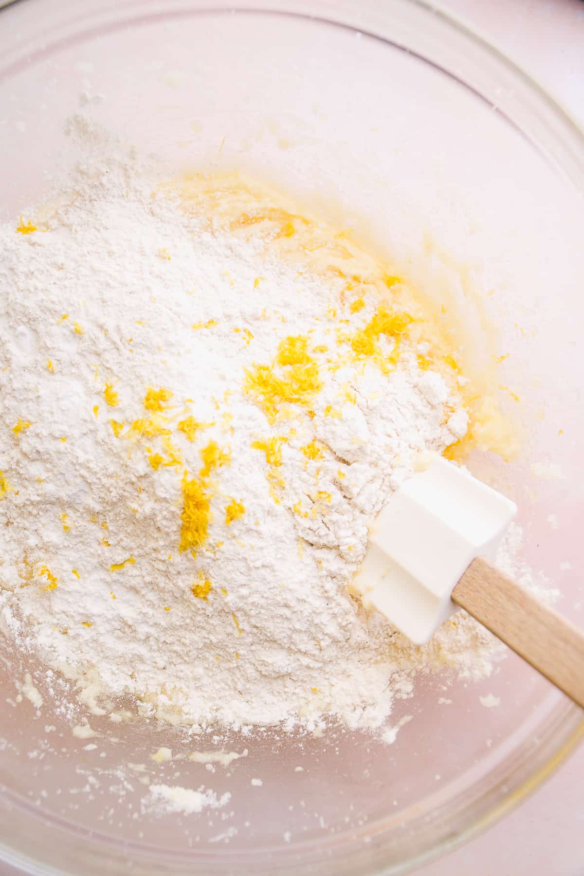 Dry ingredients about to be mixed into a glass bowl with lemon cookie dough.