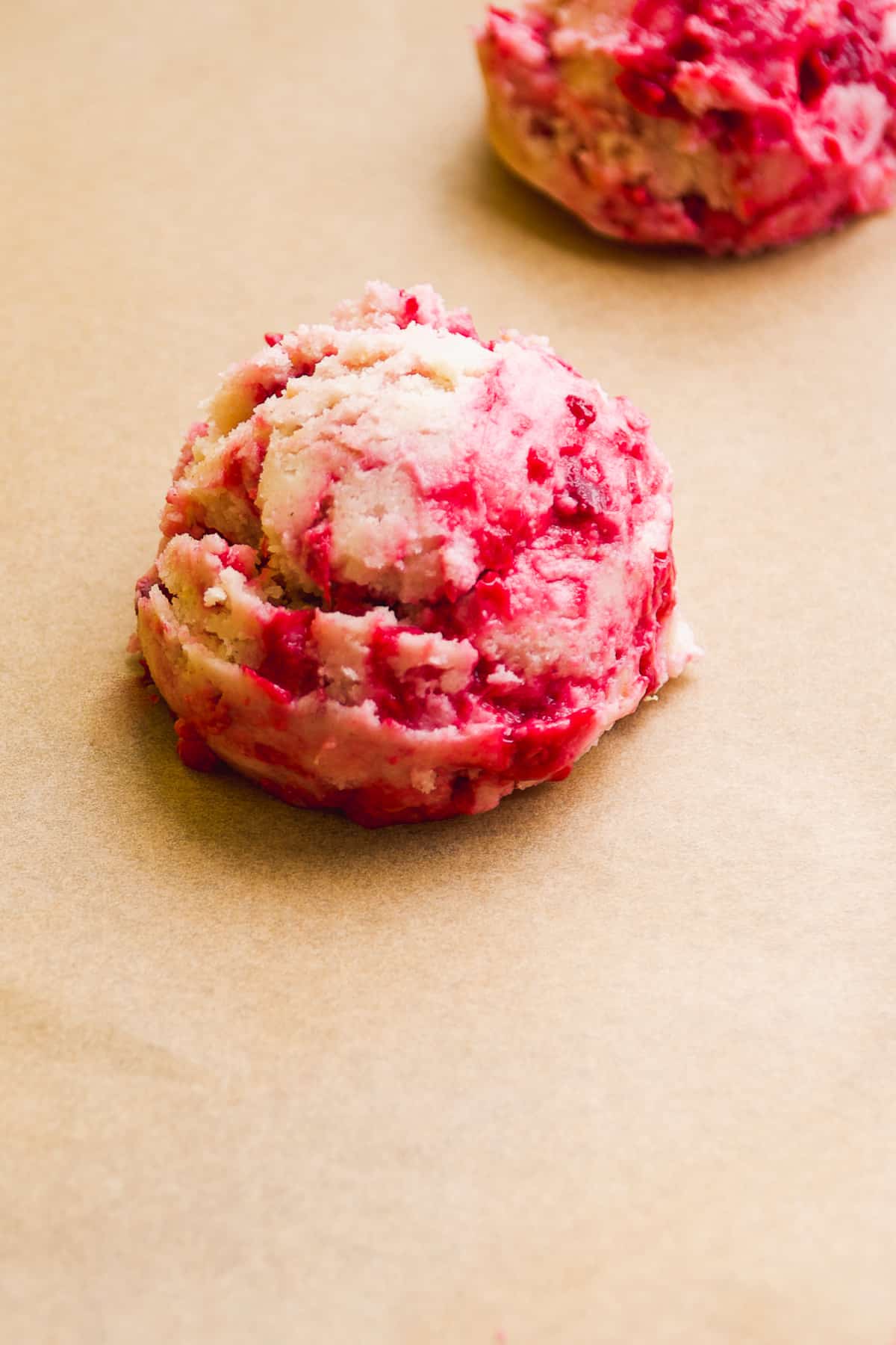 A ball of raspberry lemonade cookie dough about to be baked on a cookie sheet.