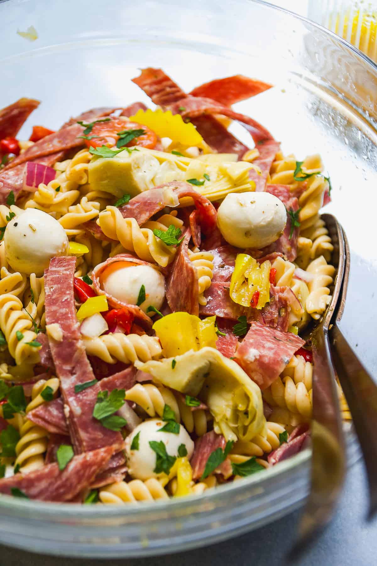 Glass bowl with zesty Italian pasta salad with noodles and cheese and vegetables.