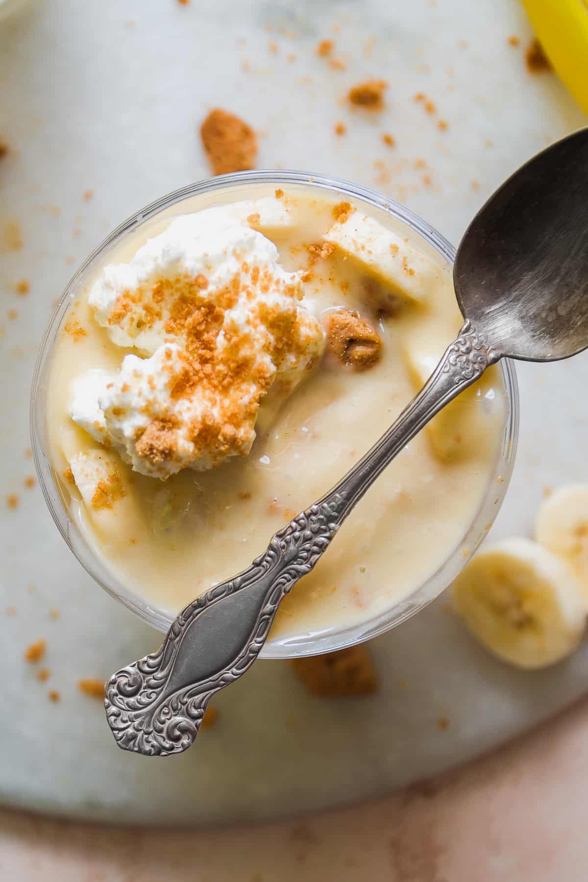 Overhead view of a glass of dairy free banana pudding with whipped cream and a spoon resting on the side.