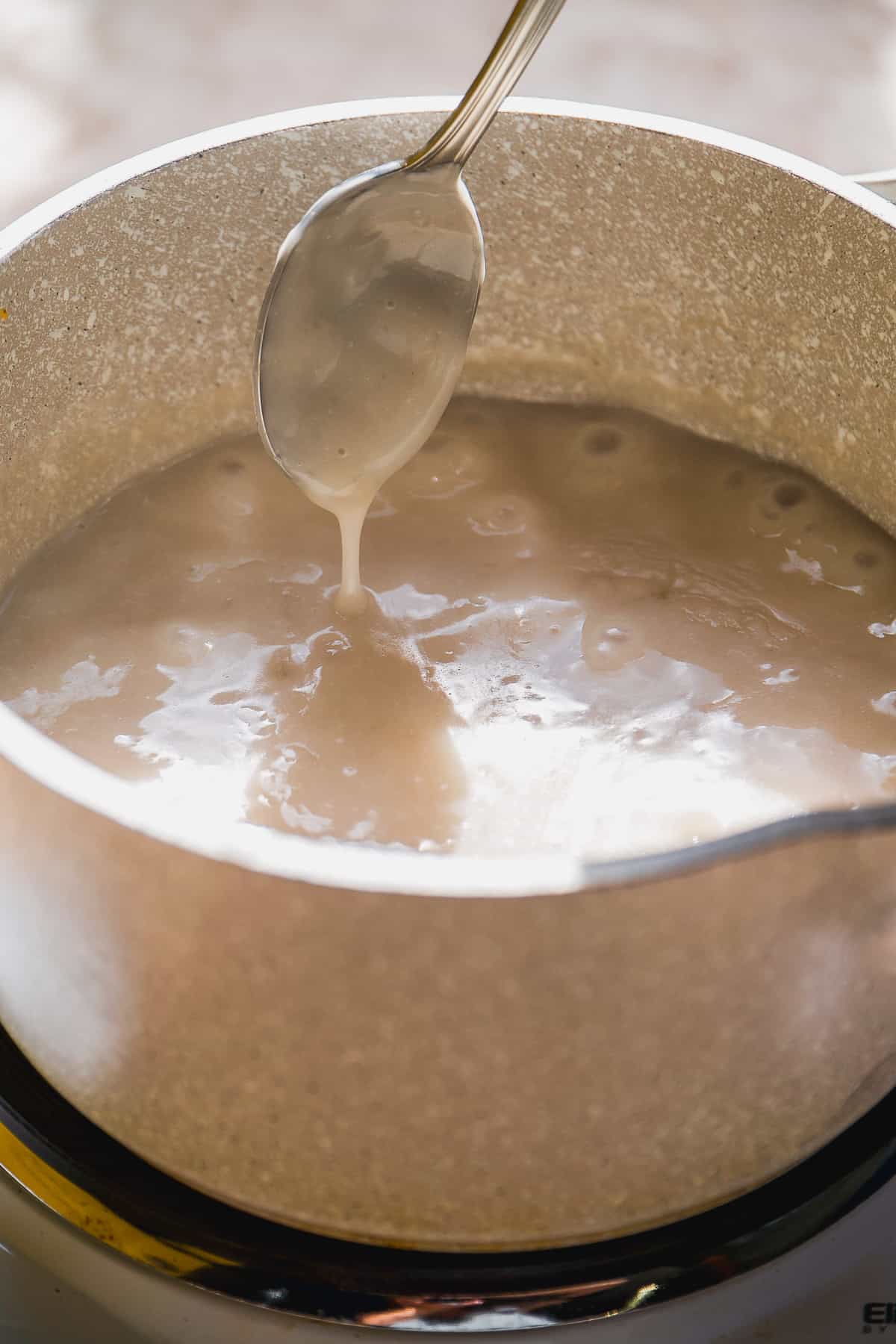 Gray pot with simmering milk and a spoon stirring.
