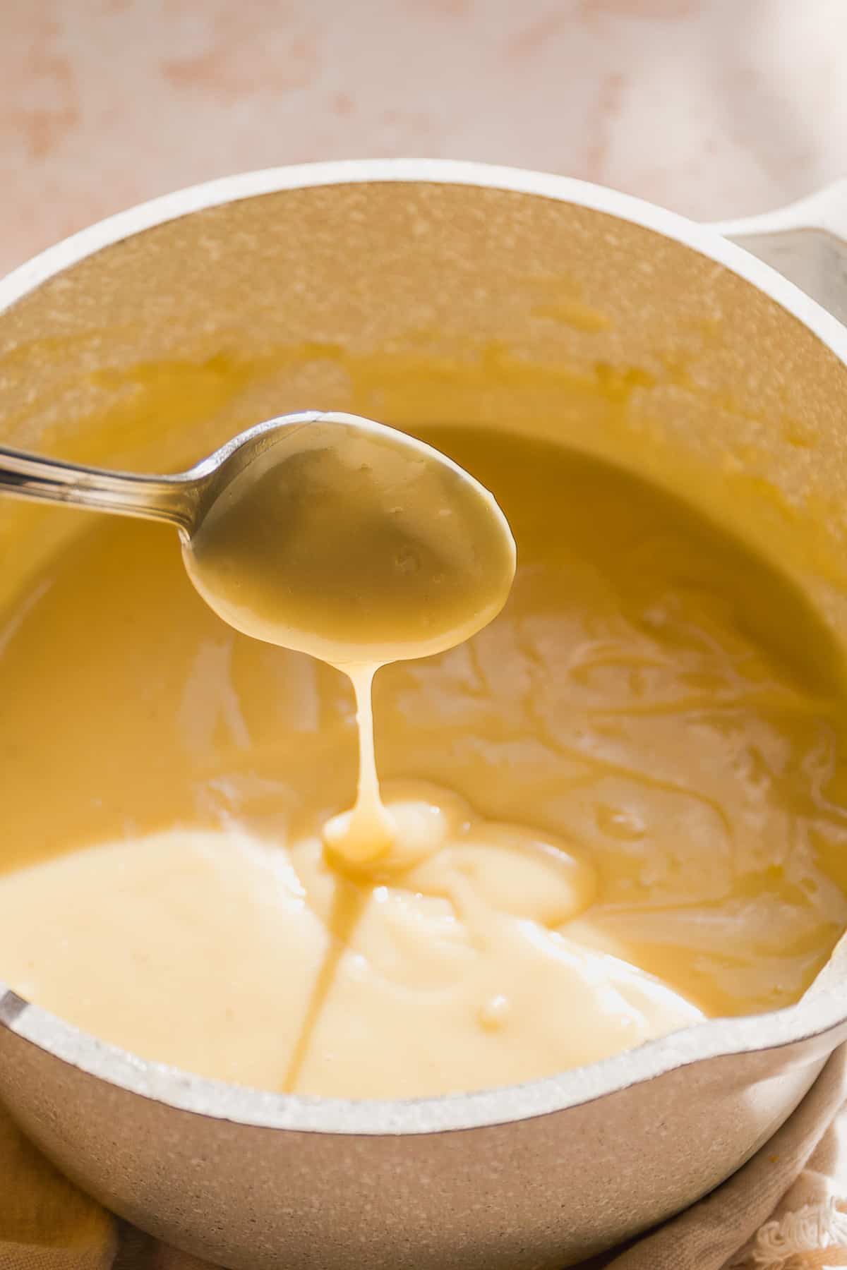 A pot with vanilla pudding and a spoon letting some run off the end.