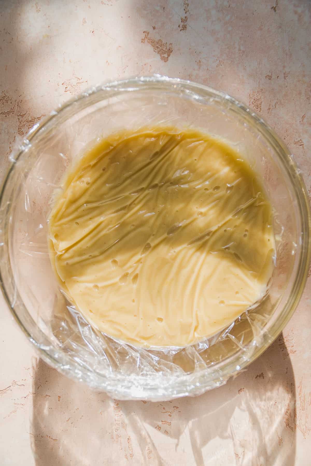 Glass bowl with banana pudding and plastic wrap over top.