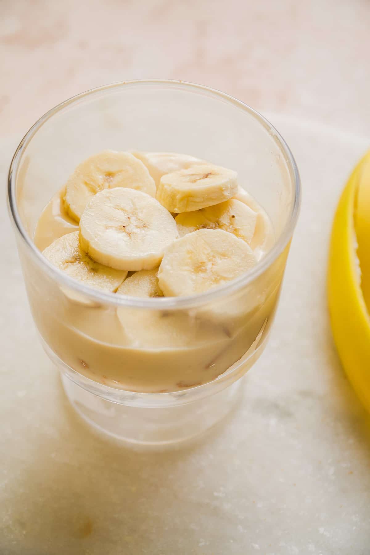 Small glass with banana pudding and a layer of sliced bananas.