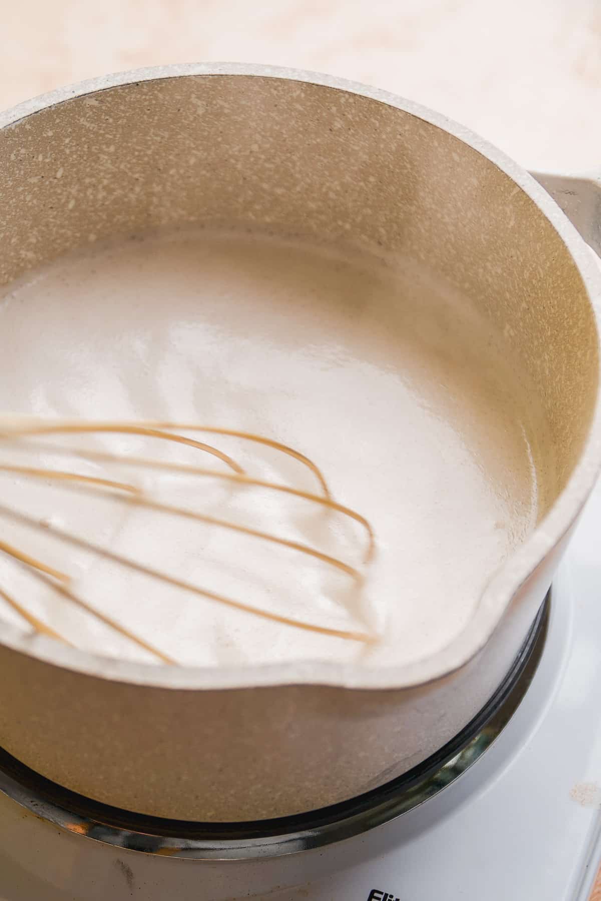 Gray pot with simmering milk inside and a whisk stirring.