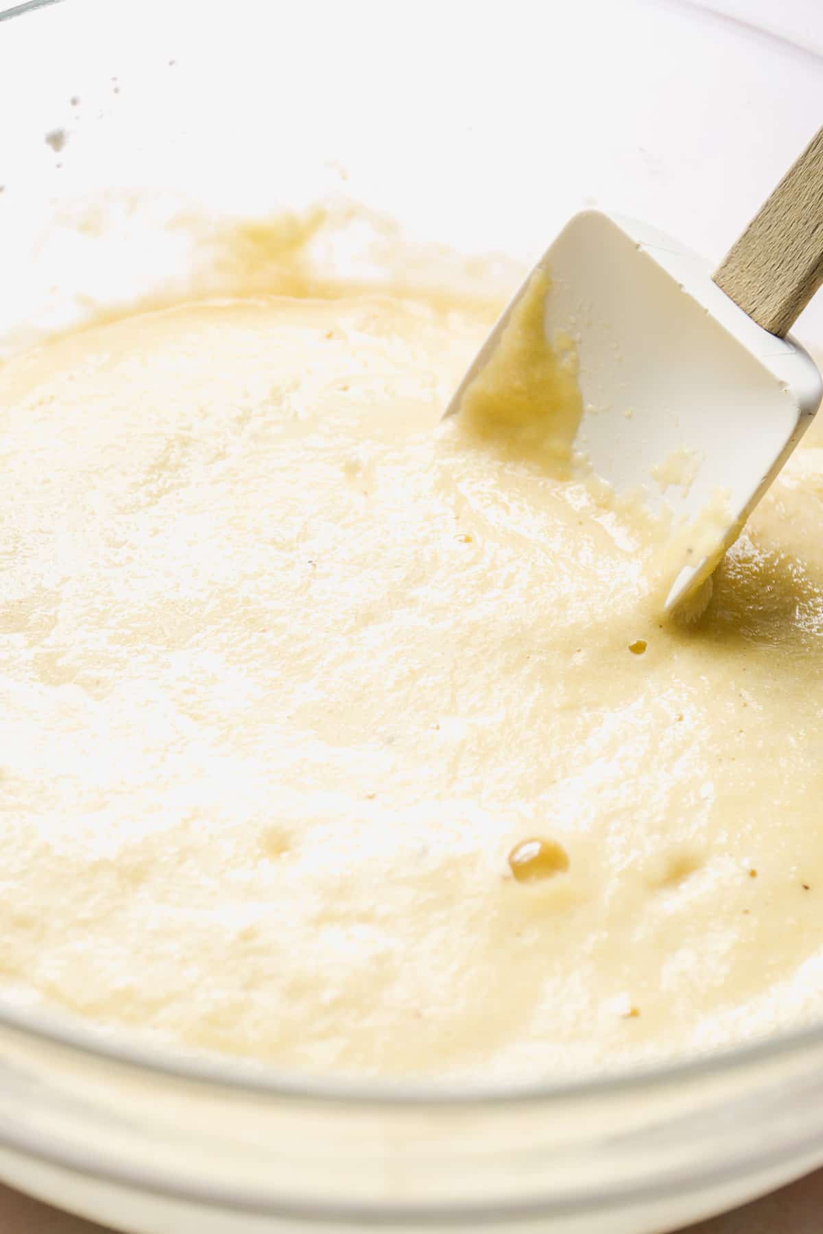 Glass bowl with muffin batter inside and a rubber spatula.