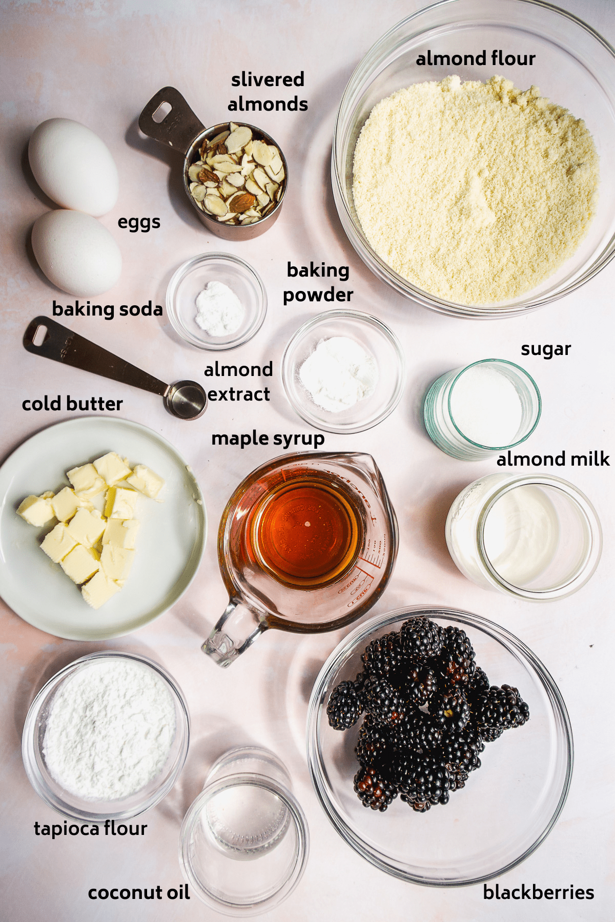 Almond flour blackberry muffin ingredients on a pink surface with labels in black.