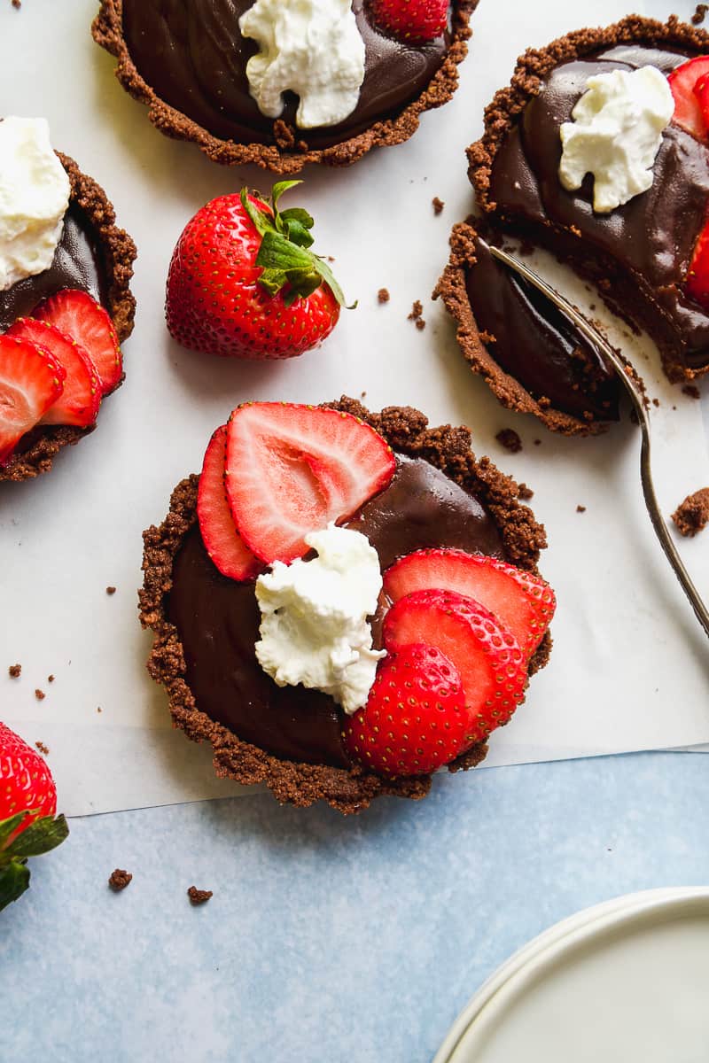 Mini chocolate tarts with strawberries and whipped cream on top.