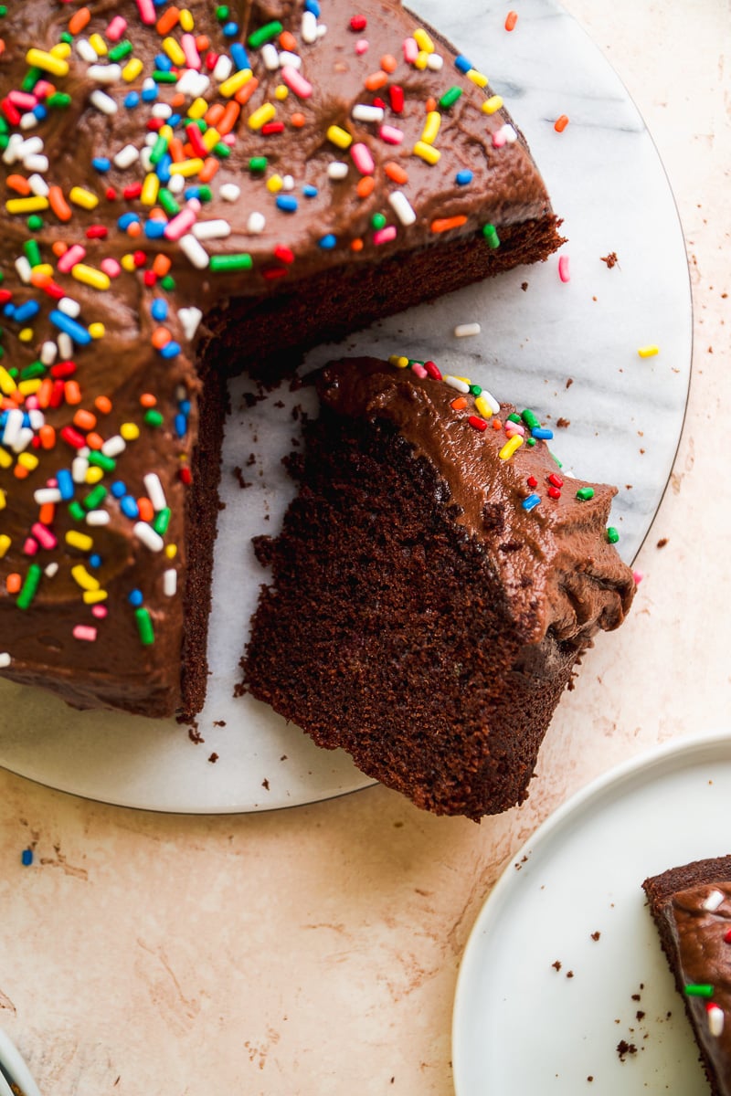 Small chocolate cake topped with sprinkles with a slice out.