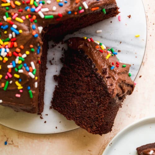 Small chocolate cake with sprinkles with a slice cut out.