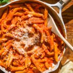 Skillet with spicy vodka pasta and a wooden spoon resting inside.