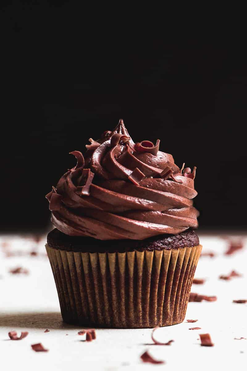 Chocolate cupcake sitting in front of a black backdrop with chocolate shavings.