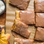 Apple pop tarts on parchment paper with cinnamon frosting.