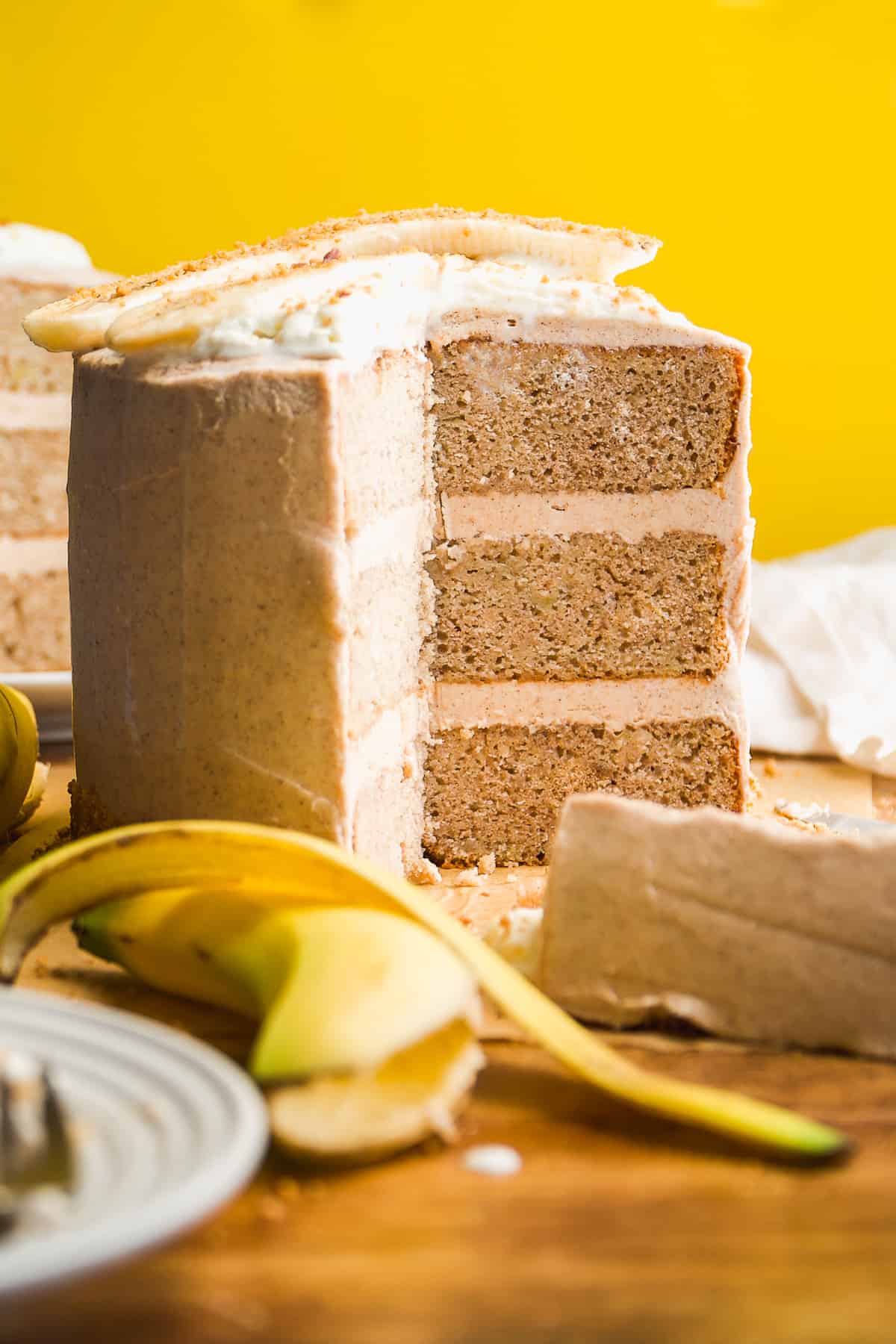 Layered banana cake with cinnamon maple icing in front of a yellow backdrop.