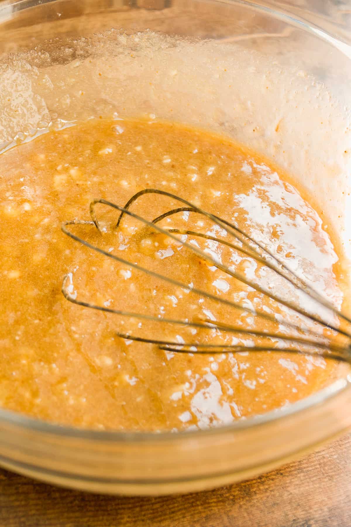 Glass bowl with wet ingredients being whisked.