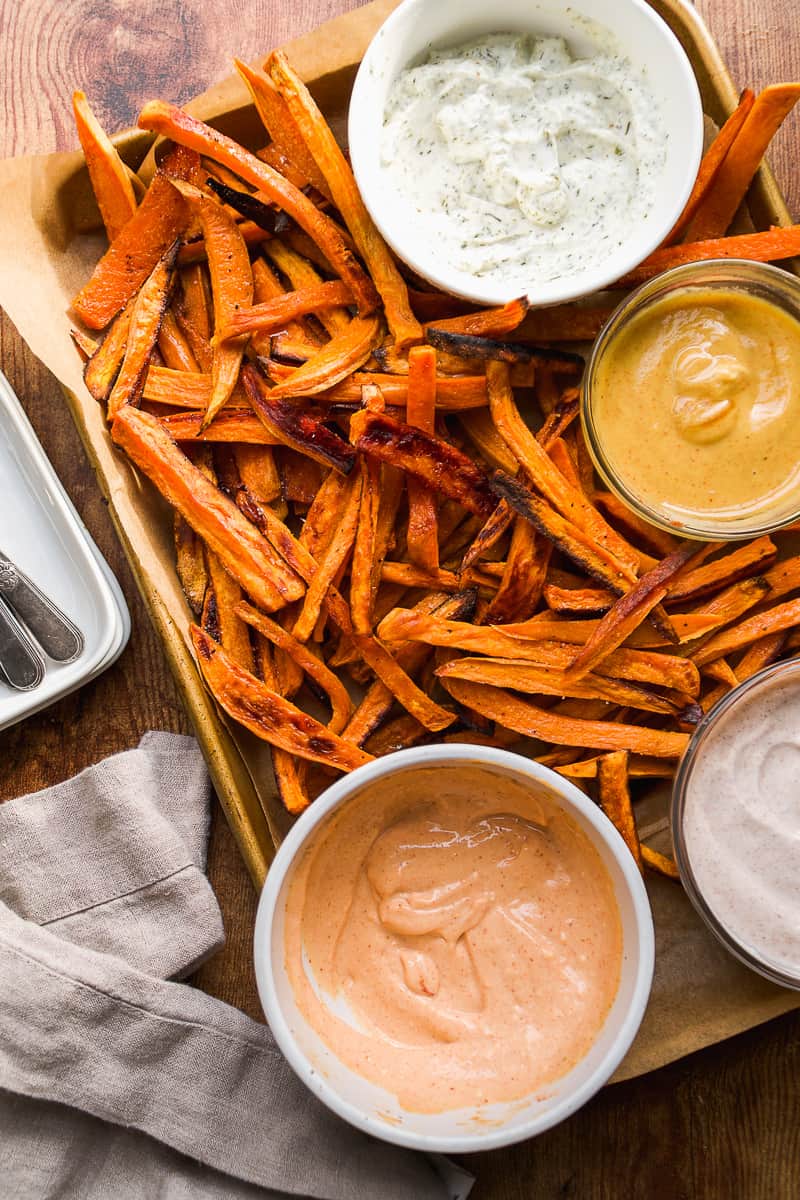 A sheet pan of sweet potato fries with four dipping sauces.