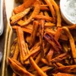 Sweet potato fries piled on a baking sheet with dipping sauces.