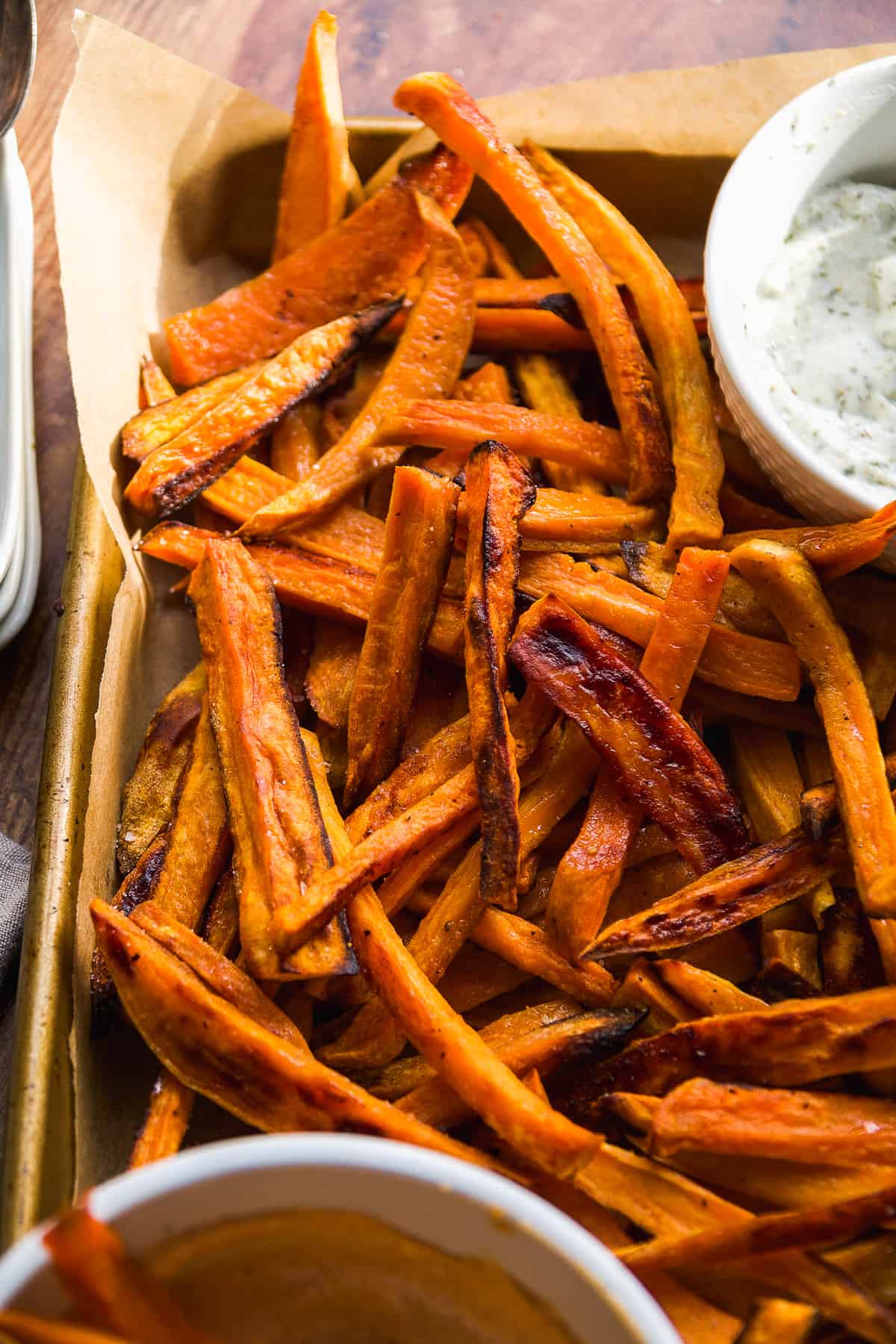 Sweet potato fries piled on a baking sheet with dipping sauces.