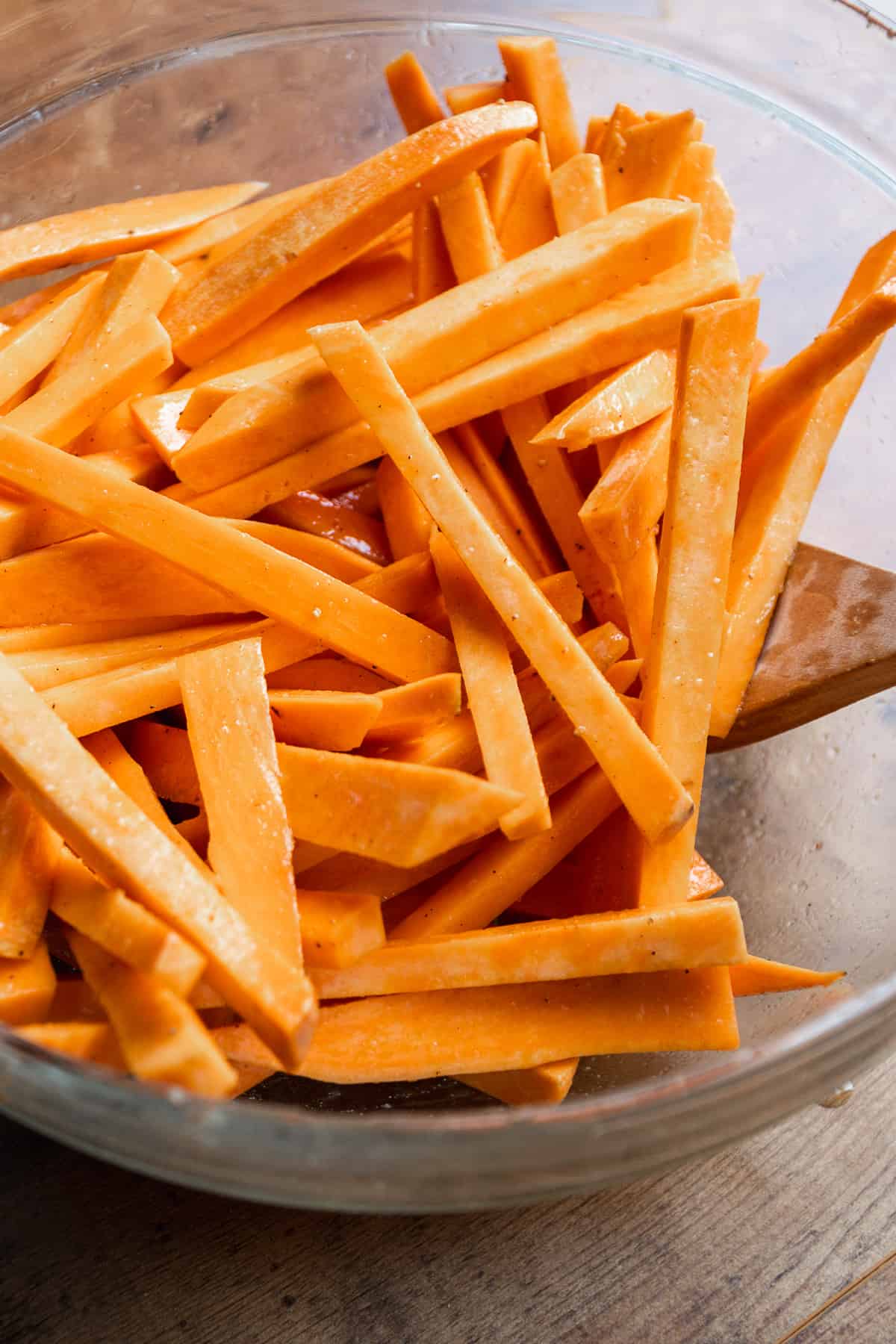 Sweet potato fries tossed in oil and spices in a glass bowl.