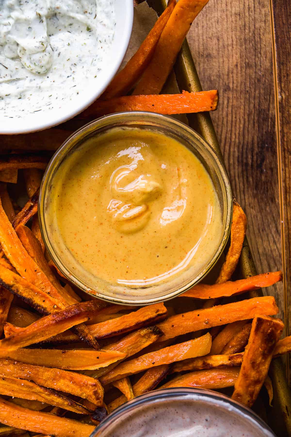 Hot honey mustard in a glass bowl on a pan of sweet potato fries.