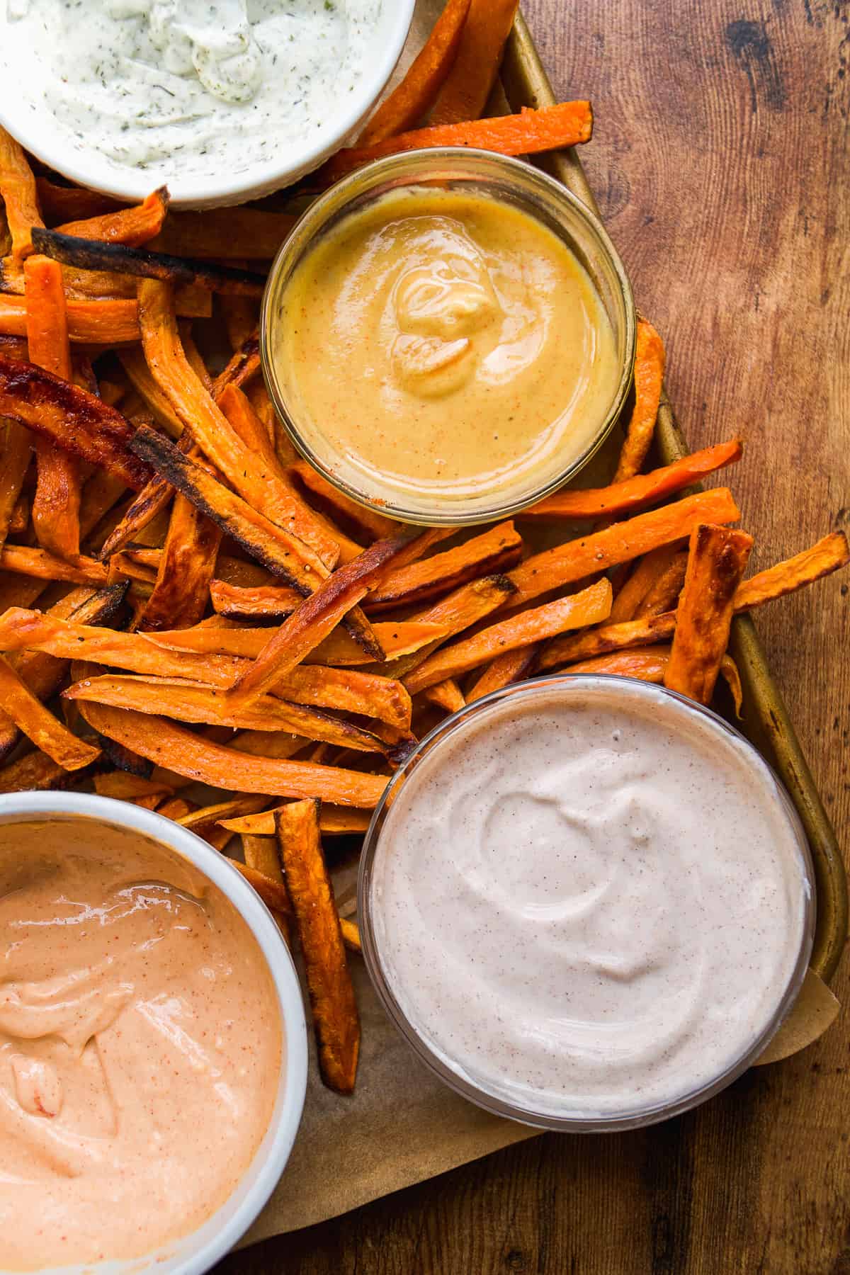 A sheet pan of sweet potato fries with four dipping sauces.