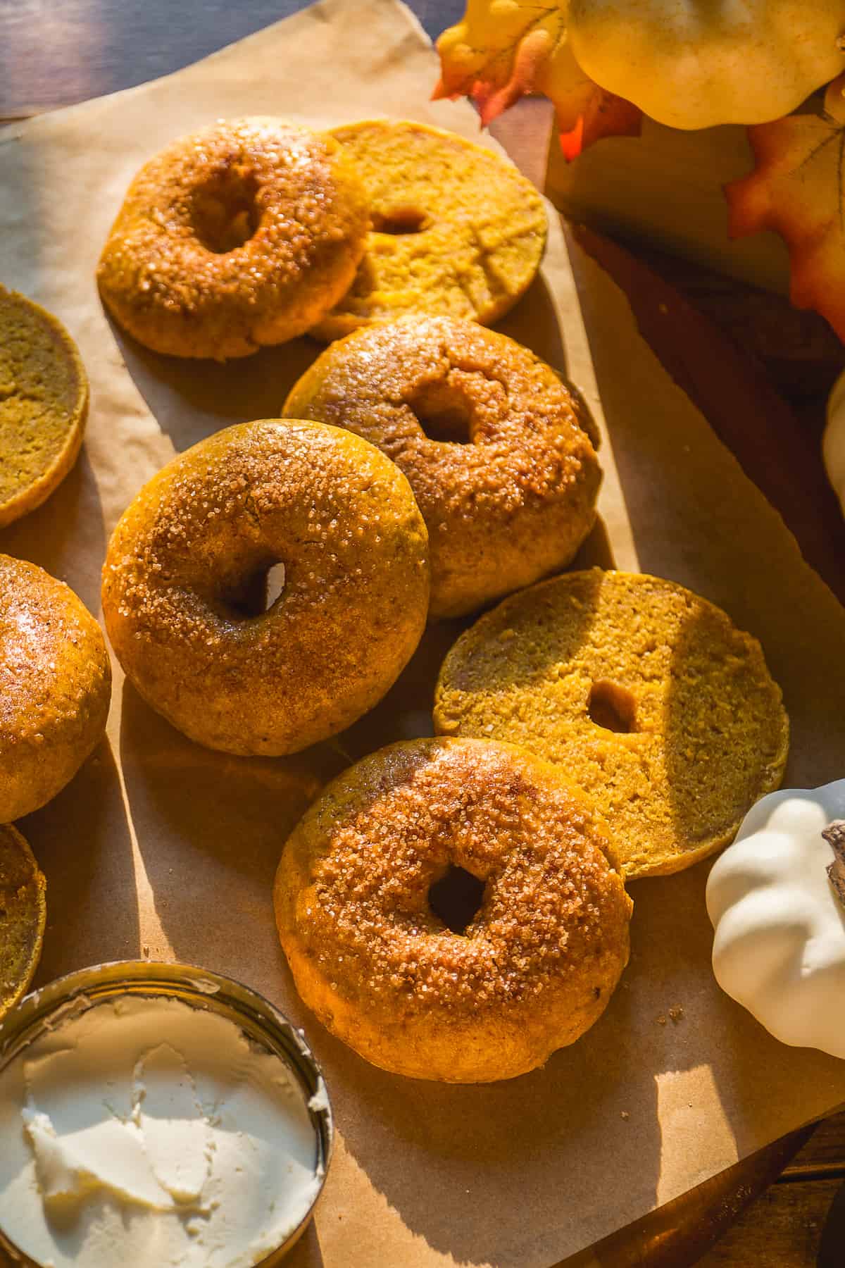 Pumpkin bagels with cinnamon sugar on top scattered on parchment paper.