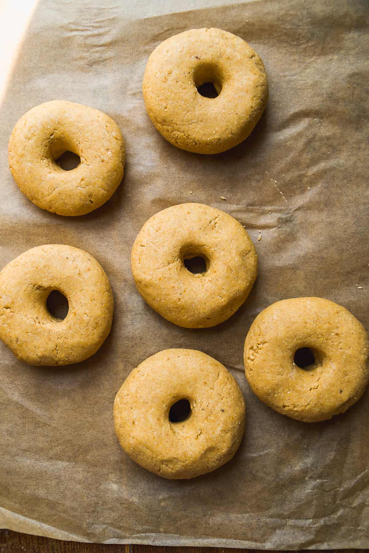 Pumpkin bagels about to be baked on parchment paper.