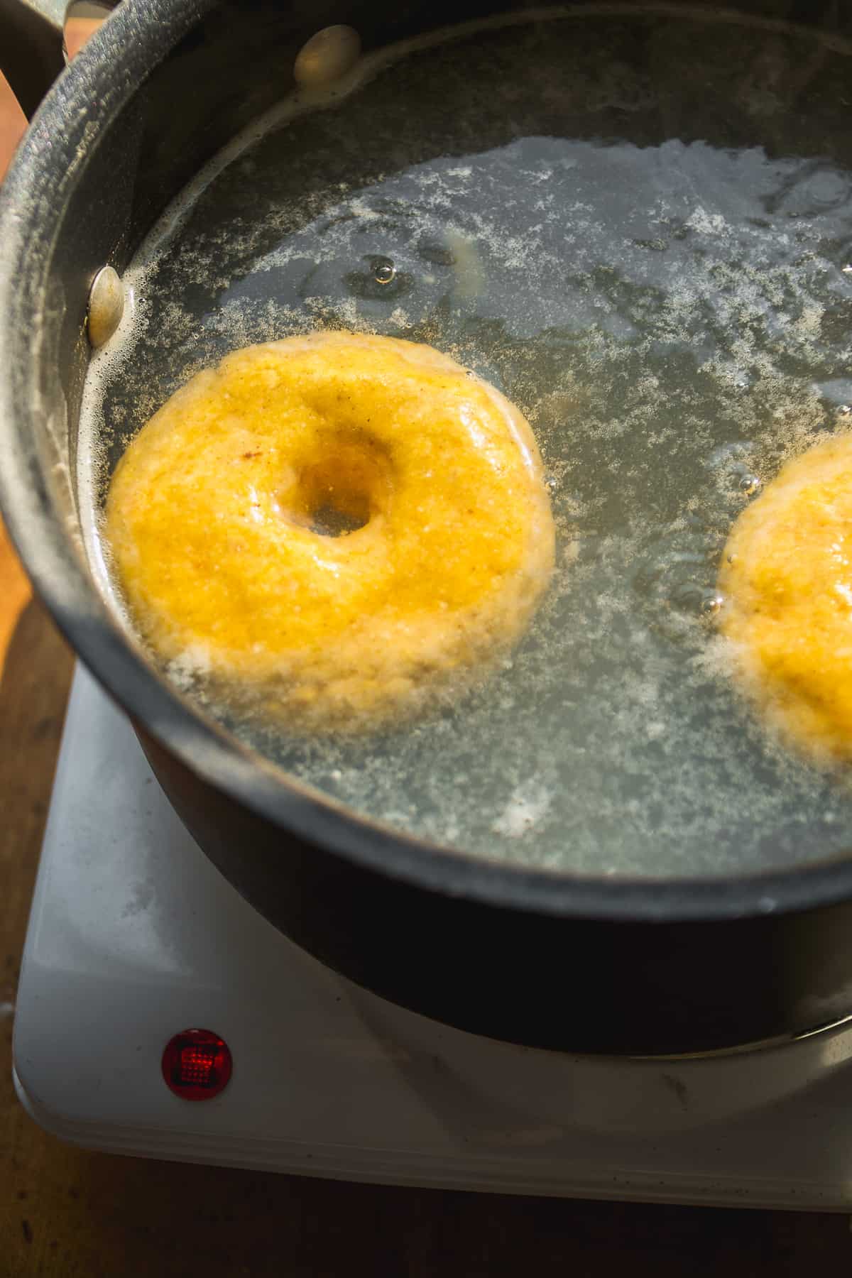 Pumpkin bagel boiling in a black pot of water.