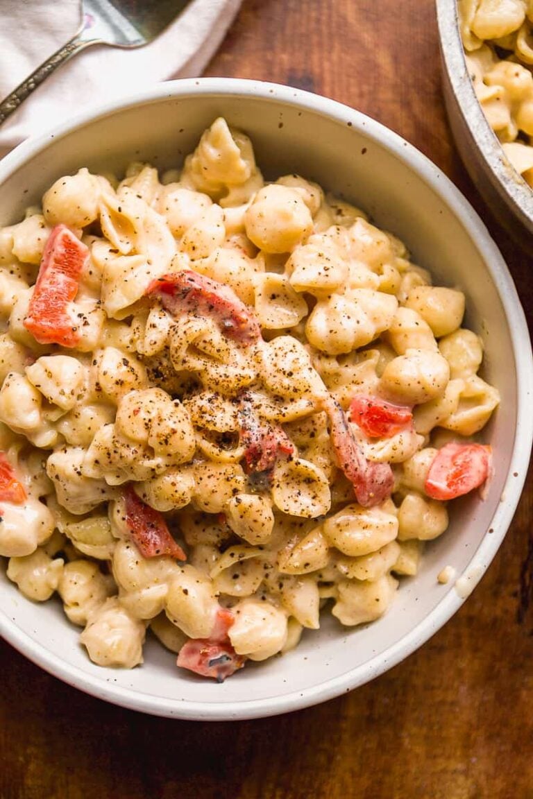 Bowl of tahini pasta with red peppers on a wooden surface.