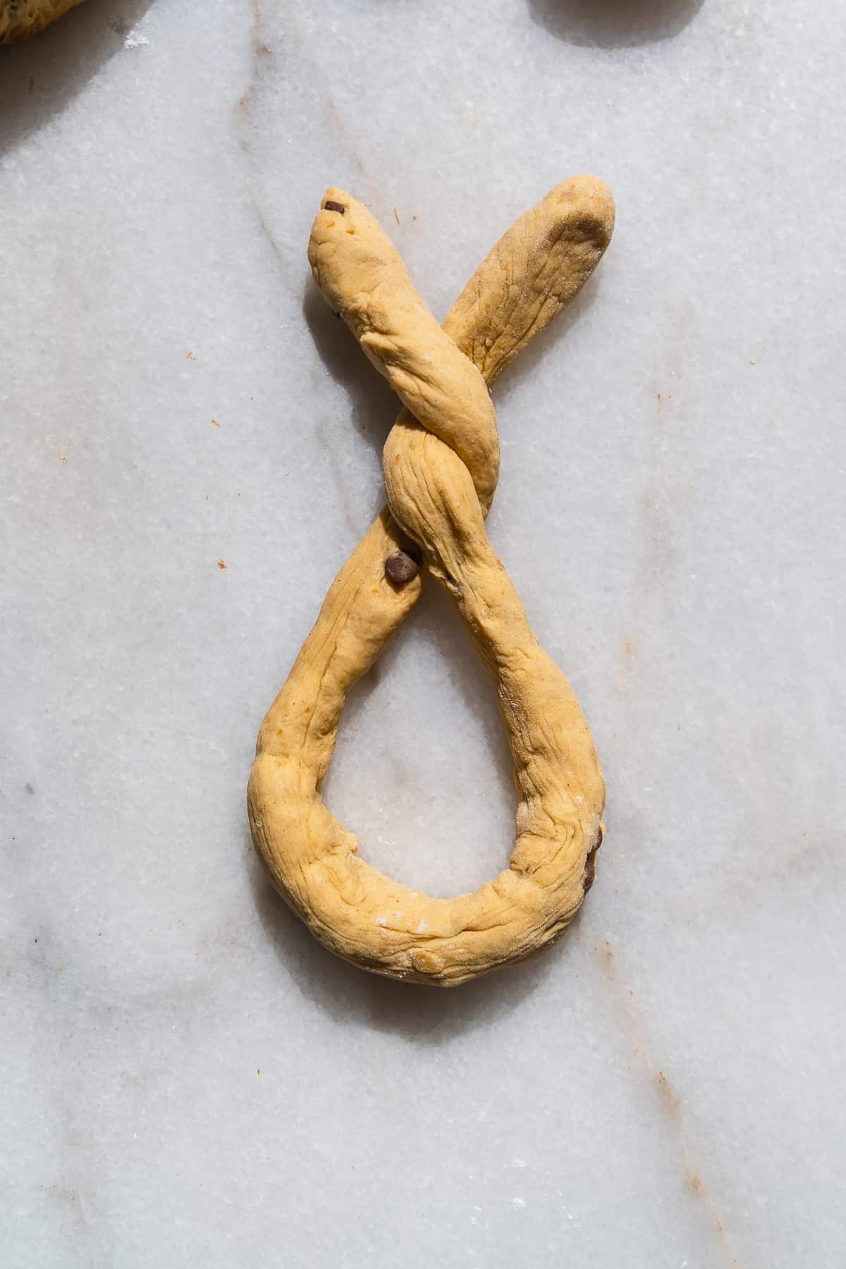 Pumpkin soft pretzel dough in a twist forming a pretzel shape.